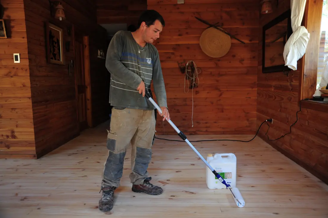 Aplicación de barniz en piso de madera de una cabaña